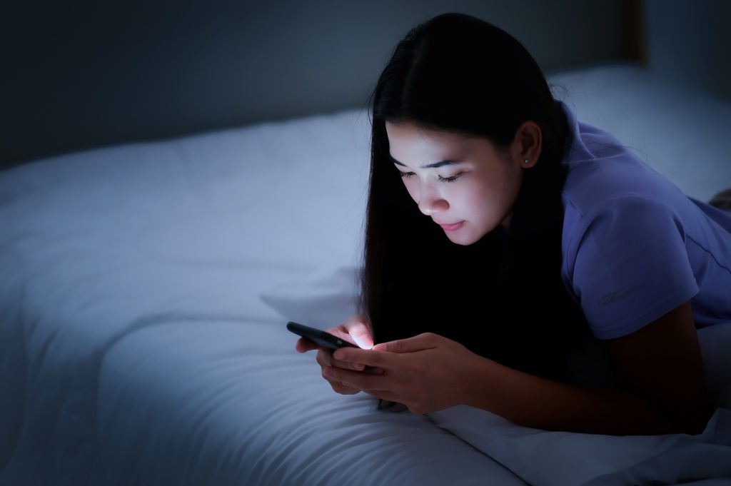 Young woman using smart phone at night in bedroom