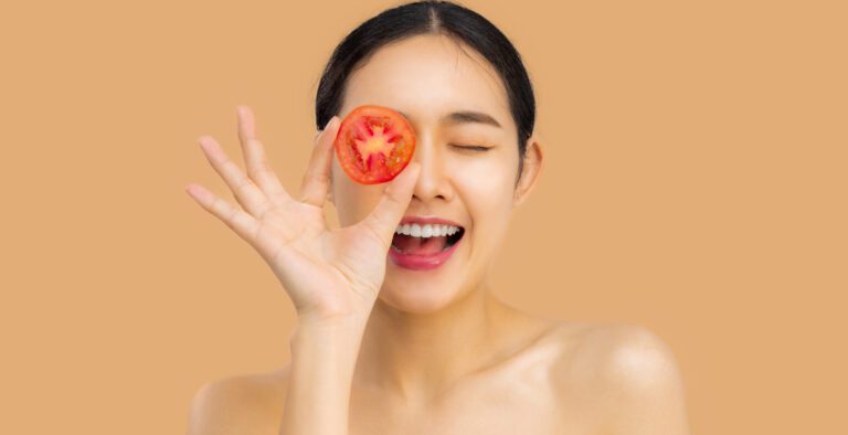 Charming beautiful young asian woman use piece of tomatoes sliced close her eyes with smiley face good health and nice skin beige background.